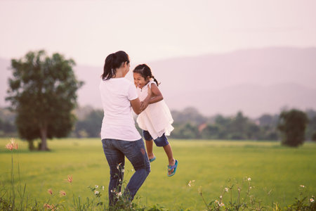 Happy mother holding her kid and spinning around with fun in the field in vintage color toneの写真素材
