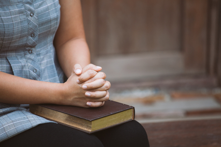 Woman hands folded in prayer on a Holy Bible  for faith concept in vintage color toneの写真素材