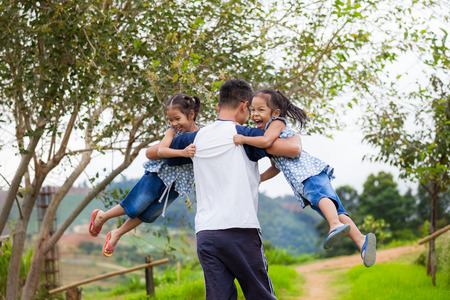 Asian father carrying two child girls and spinning around with fun in the parkの写真素材
