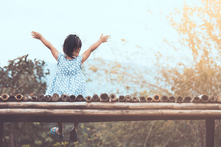 Back view of little asian child girl raise her arms sitting and looking at nature together in vintage color toneの写真素材