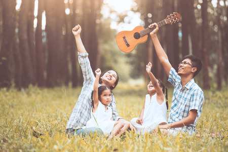 Happy family father, mother and two little child girls raise their hand and having fun together in the park in vintage color toneの写真素材