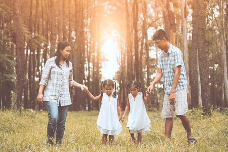 Family father, mother and two little child girls holding hand and walking together in the park at sunsetの写真素材