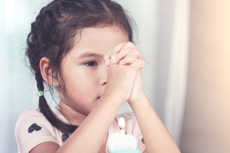 Cute asian little child girl make folded hand to wish the good things for her birthday in party in...