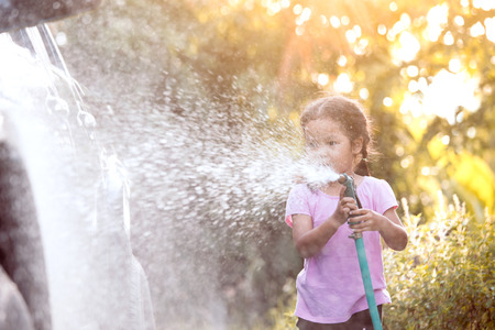 Happy asian child girl help parent washing car on water splashing with sunlightの写真素材