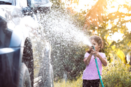 Happy asian child girl help parent washing car on water splashing with sunlightの写真素材