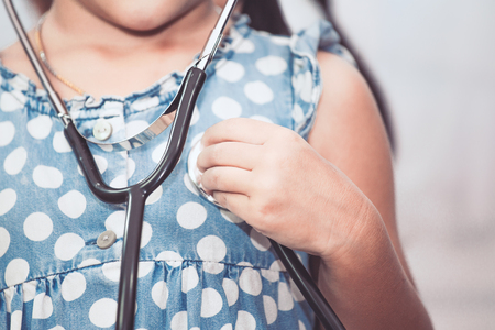 Cute asian little child girl with stethoscope playing doctor to listen her heartの写真素材