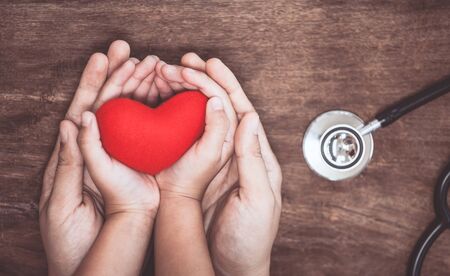 Red heart on woman and child hands and with doctor's stethoscope on wooden background. Healthcare medical  conceptの写真素材