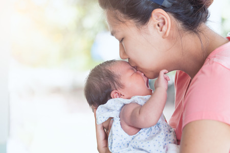 Happy asian mother hugging and kissing her newborn baby with loveの写真素材