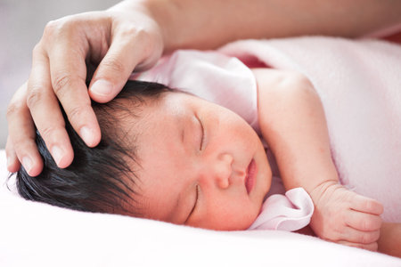 Mother hand touching asian newborn baby girl head while she sleeping with tenderness