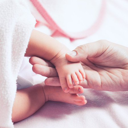 Mother hand holding newborn baby girl feet while she sleeping with love in vintage color toneの写真素材