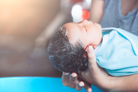 Cute asian newborn baby girl take a bath. Mom cleaning her baby hair.の写真素材