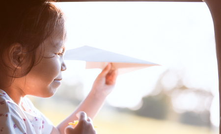 Cute asian little child girl having fun to play with toy paper airplane out of car window in the countryside in vintage color toneの写真素材
