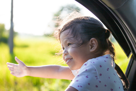 Cute asian little child girl smiling and having fun to  travel by car. Child reach out her hand and look out from car window in the countrysideの写真素材