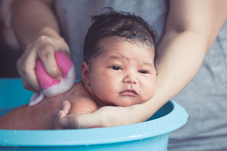 Cute asian newborn baby girl take a bath in bathtub. Mom cleaning her baby body with tendernessの写真素材