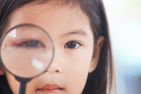 Closeup of asian child girl eye swell from bacteria virus looking through a magnifying glassの写真素材