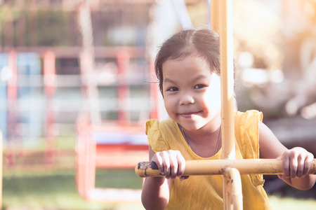Happy asian little child girl having fun to play on rocking horse in playground in vintage color toneの写真素材