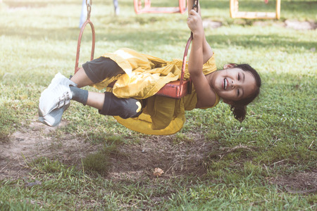 Happy asian little child girl flying on swing in playground in the sunset time in blurred motionの写真素材
