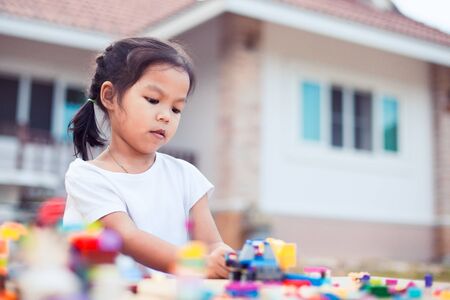 Cute asian little child girl playing with colorful blocks. She is creating and building her toy with fun in good weather outside.の写真素材