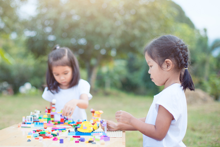 Two cute asian little child girl playing with colorful blocks together. They are creating and building their toy with fun in good weather outside.の写真素材