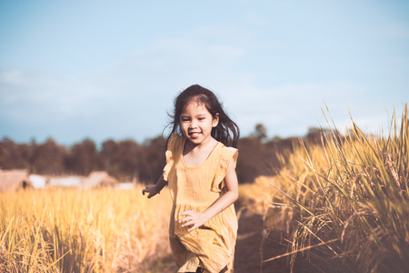 Cute asian child girl having fun to run in the cornfield in vintage color toneの写真素材