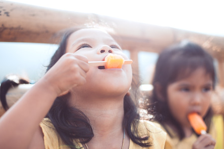 Cute asian little child girl is eating icecream with her sister in the parkの写真素材