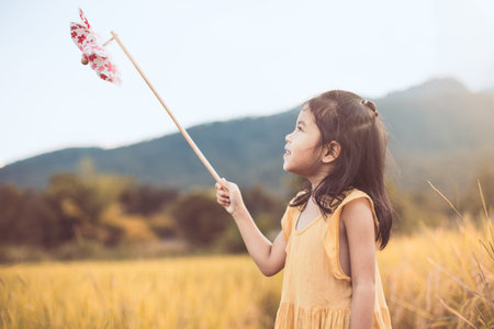 Cute asian little child girl playing with wind turbine in the paddy field in vintage color toneの写真素材