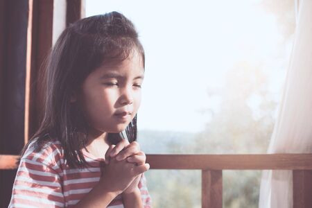 Cute asian little child girl praying with folded her hand in the room for faith,spirituality and religion conceptの写真素材