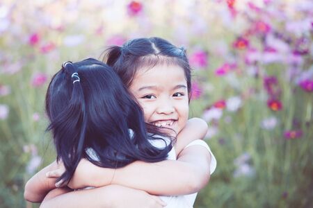 Two asian little girls hugging each other with love in the cosmos flower field in  vintage color toneの写真素材