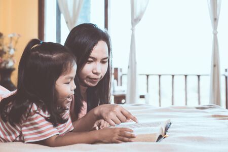 Happy family asian mother and daughter read a book together in the bedroom in vintage color toneの写真素材