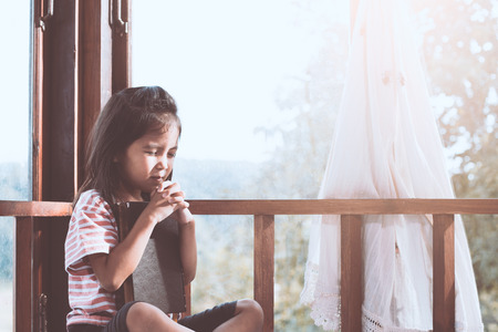 Cute asian little child girl praying with folded her hand in the room for faith,spirituality and religion conceptの写真素材