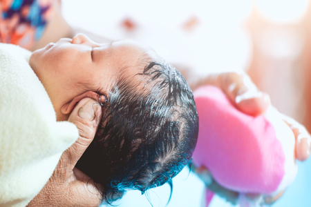Cute asian newborn baby girl take a bath. Mom cleaning her baby hair with sponge.の写真素材