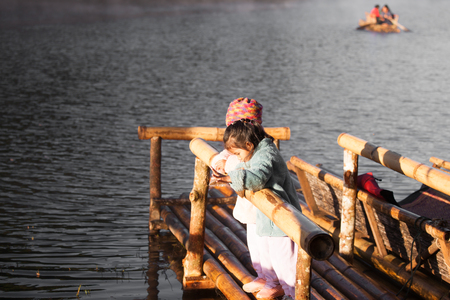 Two cute asian little child girls having fun to feed and give food to fish in the lake together with sunlight in winterの写真素材