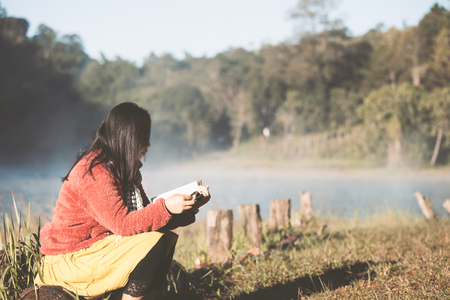 Young woman reading a book in the nature park with freshness in the morning with sunlight in vintage color toneの写真素材