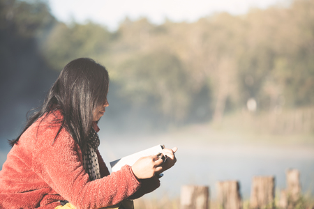 Young woman reading a book in the nature park with freshness in the morning with sunlight in vintage color toneの写真素材