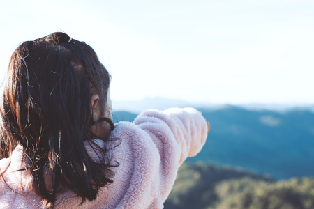 Back view of little asian child girl put on coat raise her arm and pointing to beautiful nature in winterの写真素材