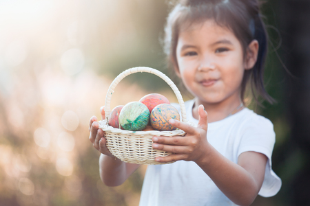 Happy asian child girl holding basket with colorful Easter eggs in outdoorの写真素材