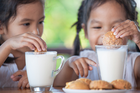 Two cute asian little child girls are eating cookies with milk for breakfast together with happinessの写真素材