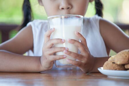 Cute asian little child girl is drinking a milk from glass with cookies for breakfastの写真素材