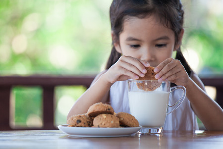 Cute asian little child girl eating cookie with milk for breakfast with happinessの写真素材