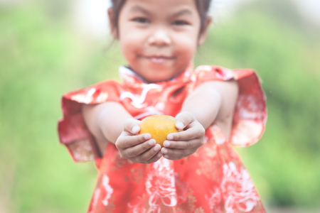 Cute asian child girl in china traditional dress holding an orange and giving you a happy in Chinese New Yearの写真素材