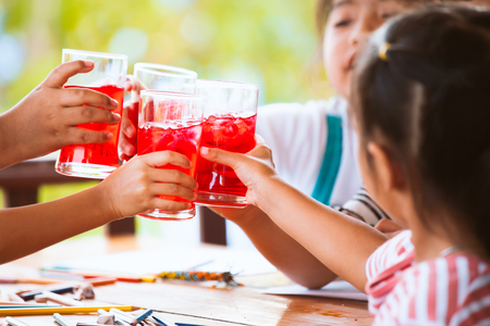 Group of asian children clinking glasses of fresh red juice water with ice and drinking together after finish their homework in the summer timeの写真素材