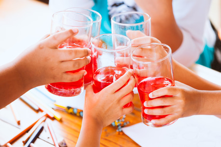 Group of asian children clinking glasses of fresh red juice water with ice and drinking together after finish their homework in the summer timeの写真素材