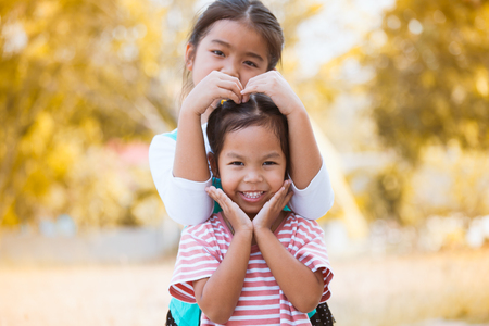 Happy asian little child girl making hand in heart shape with her sister with love and fun in the parkの写真素材