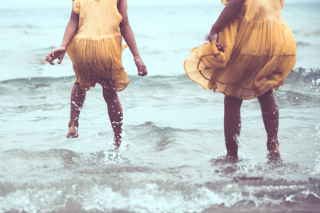 Leg of two asian little child girls jumping and playing on beach together in summer vacation in vintage color toneの写真素材