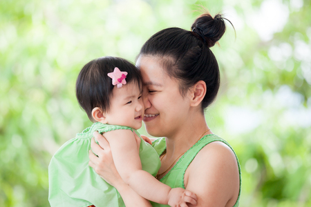 Young asian mother carrying and kissing her daughter with love and happiness on green nature backgroundの写真素材