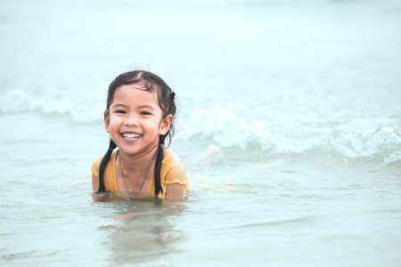 Happy asian little child girl having fun to play water in the sea in summer vacationの写真素材