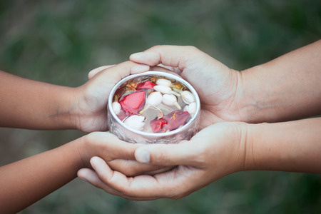 Asian little child girl and mother holding a little bowl that have flower leaf in water together for pouring on hands of elderly to respect grandparents for celebrate Songkran in new yearの写真素材