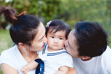 Asian family father and mother kissing daughter and playing together in the park with love and happinessの写真素材