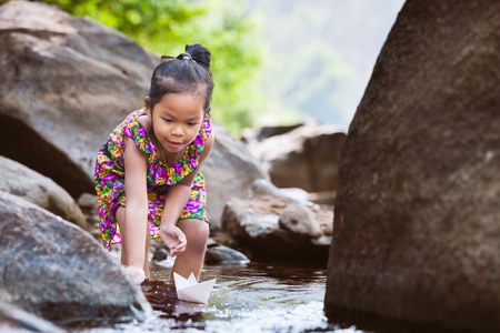 Cute asian little child girl playing paper boat in the riverside in summer time with fun and happinessの写真素材