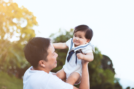 Asian father carrying his daughter up in the air and playing together in the park with fun and loveの写真素材